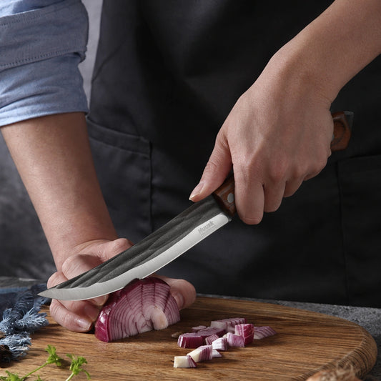Cook chopping red onion with a Huusk forged chef knife on a wooden cutting board.