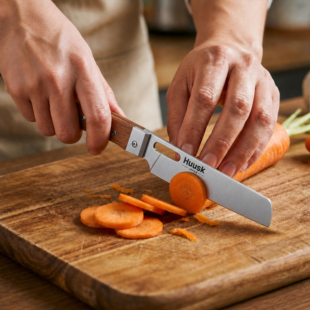 Huusk natural wood folding cleaver slicing a carrot on a kitchen cutting board.