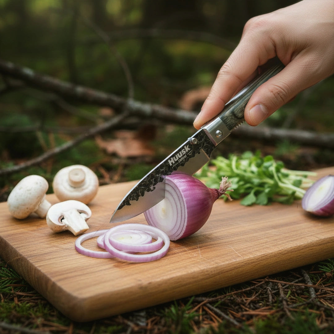 Huusk camo folding chef knife slicing red onion at an outdoor campsite.