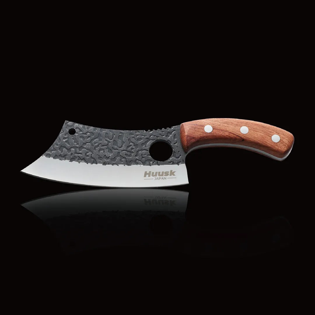 Huusk hand-forged chef knife with hammered blade, finger hole, and wood handle on black.