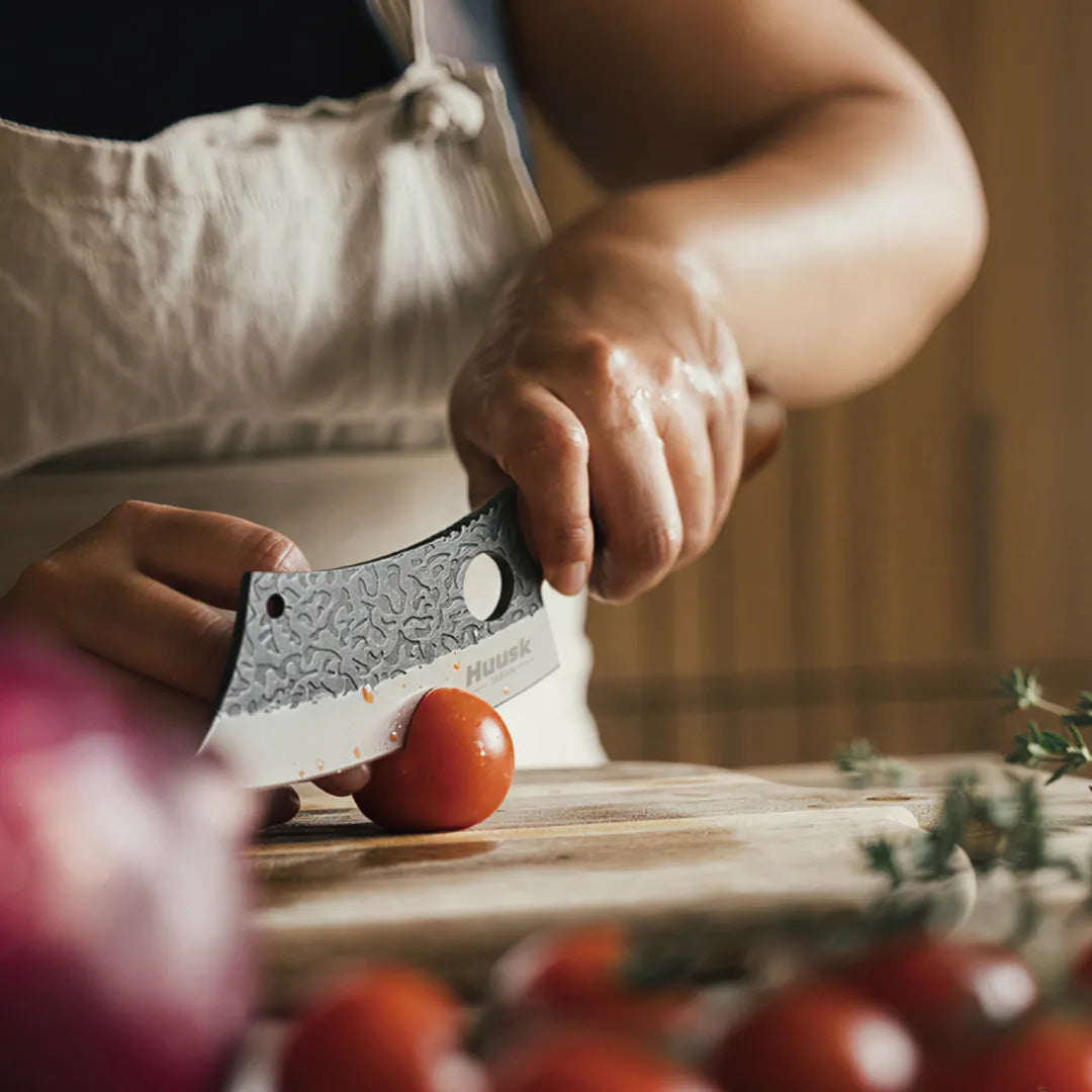Cook chopping a tomato with the Huusk hand-forged chef knife on a kitchen board.