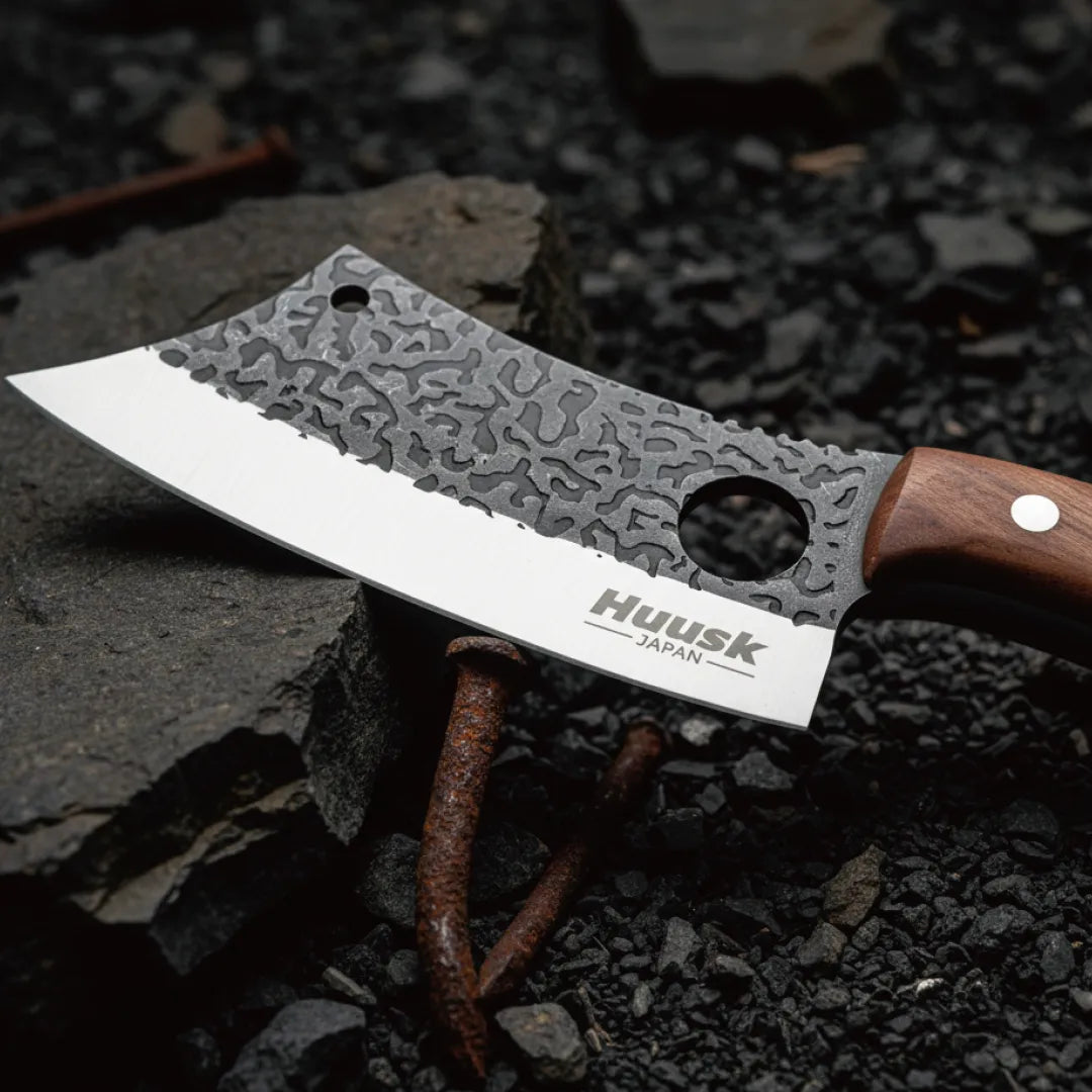 Close-up of the Huusk chef knife's hammered blade and polished edge over charcoal.