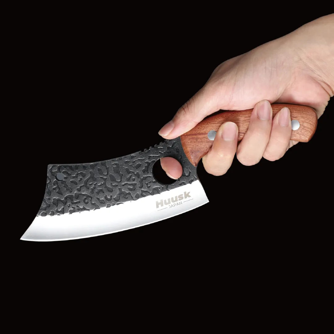 Hand holding the Huusk forged chef knife against black to show grip and scale.