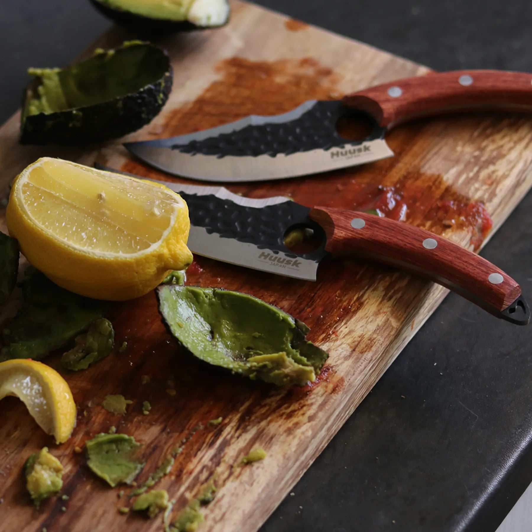 Huusk forged utility knife beside lemon, herbs, and avocado on a wooden cutting board.